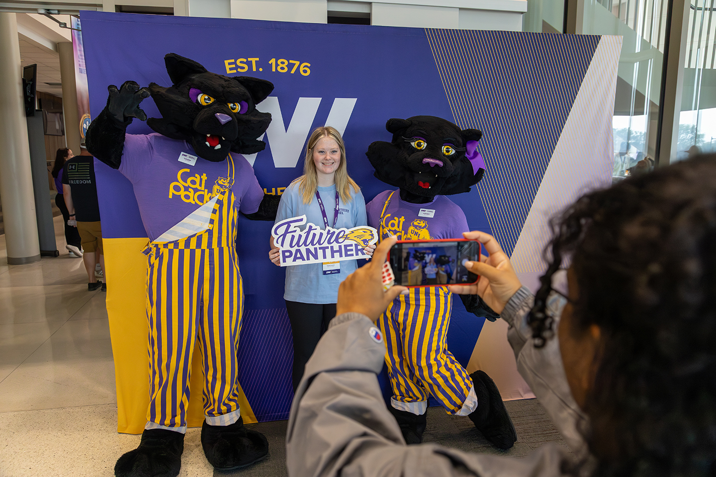 A student visiting campus posing with a sign that reads "Future Panther" alongside TC and TK Panther mascots