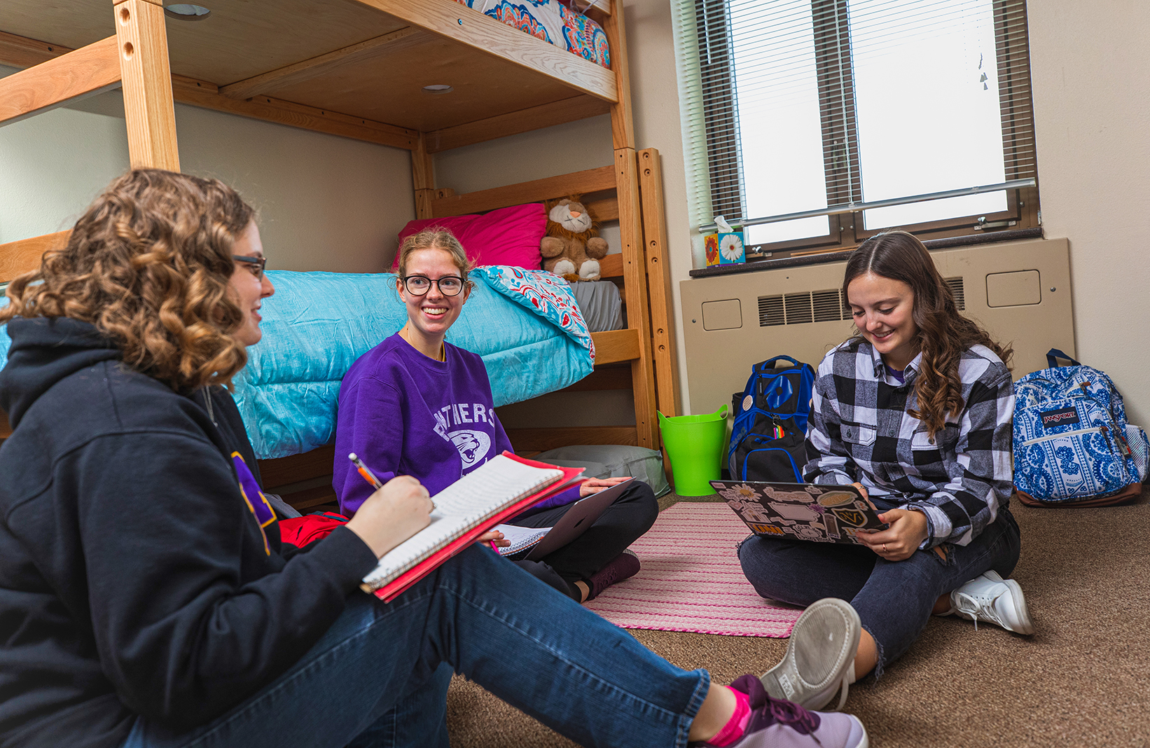 Group of three female students interacting and studying together in dorm room.