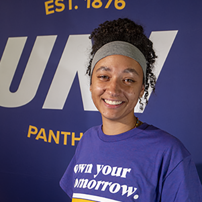 Ainsley smiling in a purple t-shirt that reads "own your tomorrow."