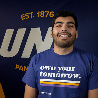 Alex smiling in a purple t-shirt that reads "own your tomorrow."