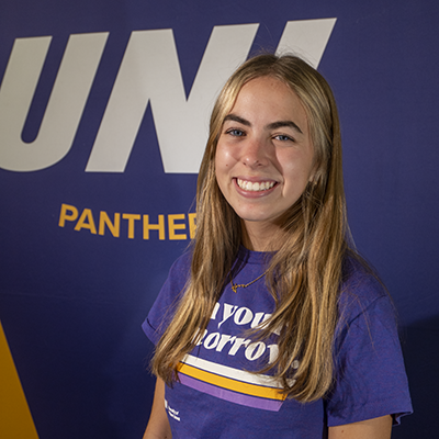 Anna smiling in a purple t-shirt that reads "own your tomorrow."