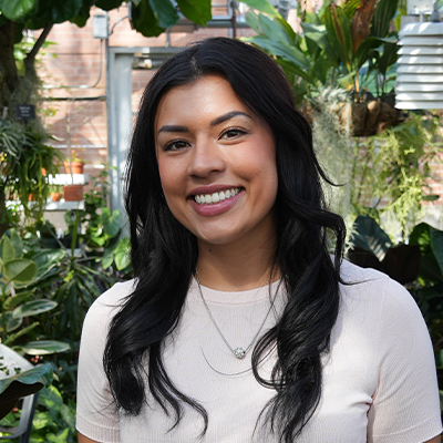 Colleen smiling with a plant-filled greenhouse behind her