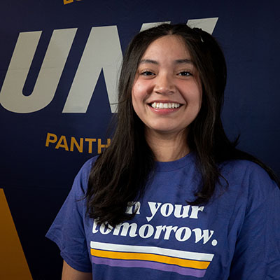 Estefany smiling in a purple t-shirt that reads "own your tomorrow."
