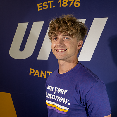 Greyson smiling in a purple t-shirt that reads "own your tomorrow."