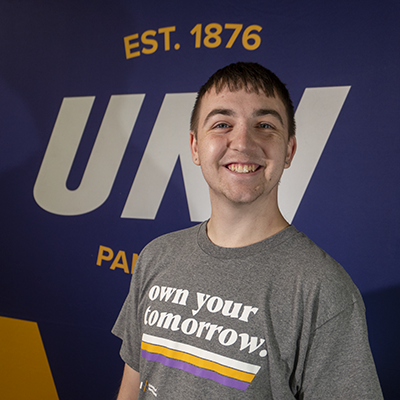 Lane smiling in a gray t-shirt that reads "own your tomorrow."