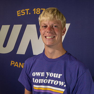 Lane smiling in a purple t-shirt that reads "own your tomorrow."