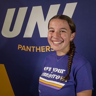 Maddy smiling in a purple t-shirt that reads "own your tomorrow."
