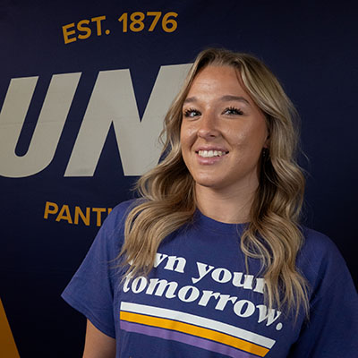 Megan smiling in a purple t-shirt that reads "own your tomorrow."