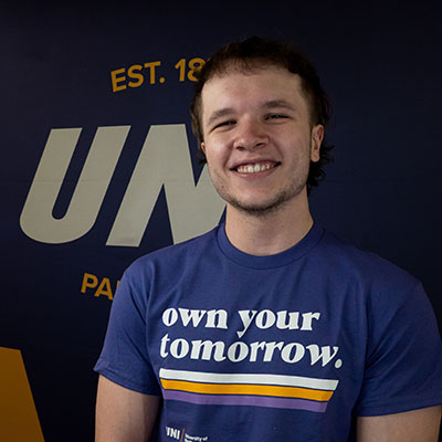 Nathan smiling in a purple t-shirt that reads "own your tomorrow."