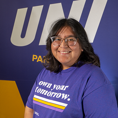 Yesi smiling in a purple t-shirt that reads "own your tomorrow."