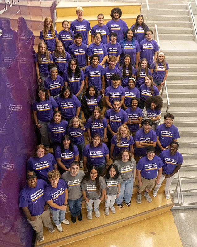 Full group of Panther Ambassadors stand together wearing purple t-shirts that read "own your tomorrow."