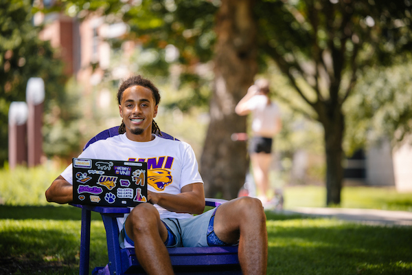 UNI student sitting in an Adirondack chair on campus with his laptop.