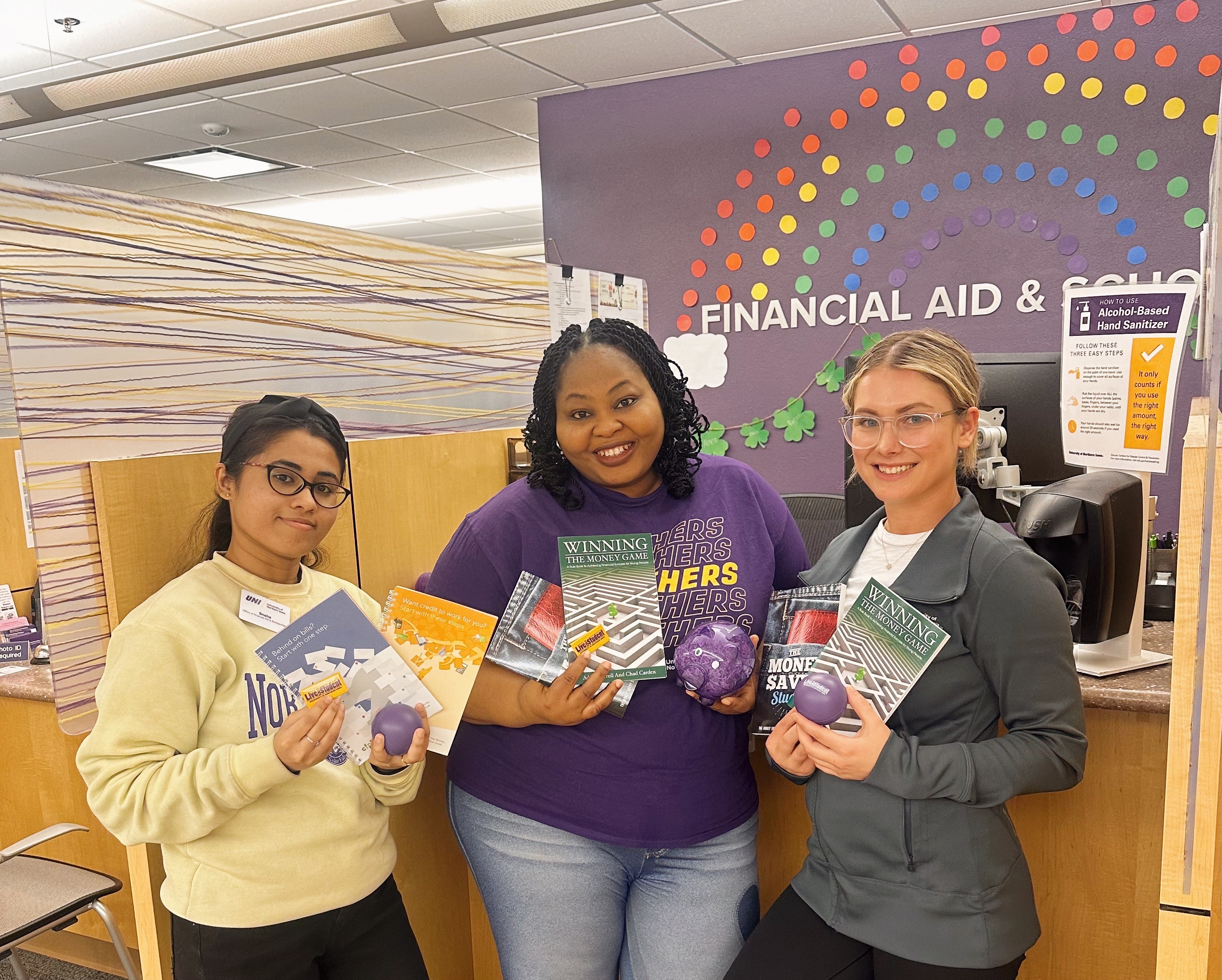 Three financial aid staff members standing in front of desk with financial aid swag