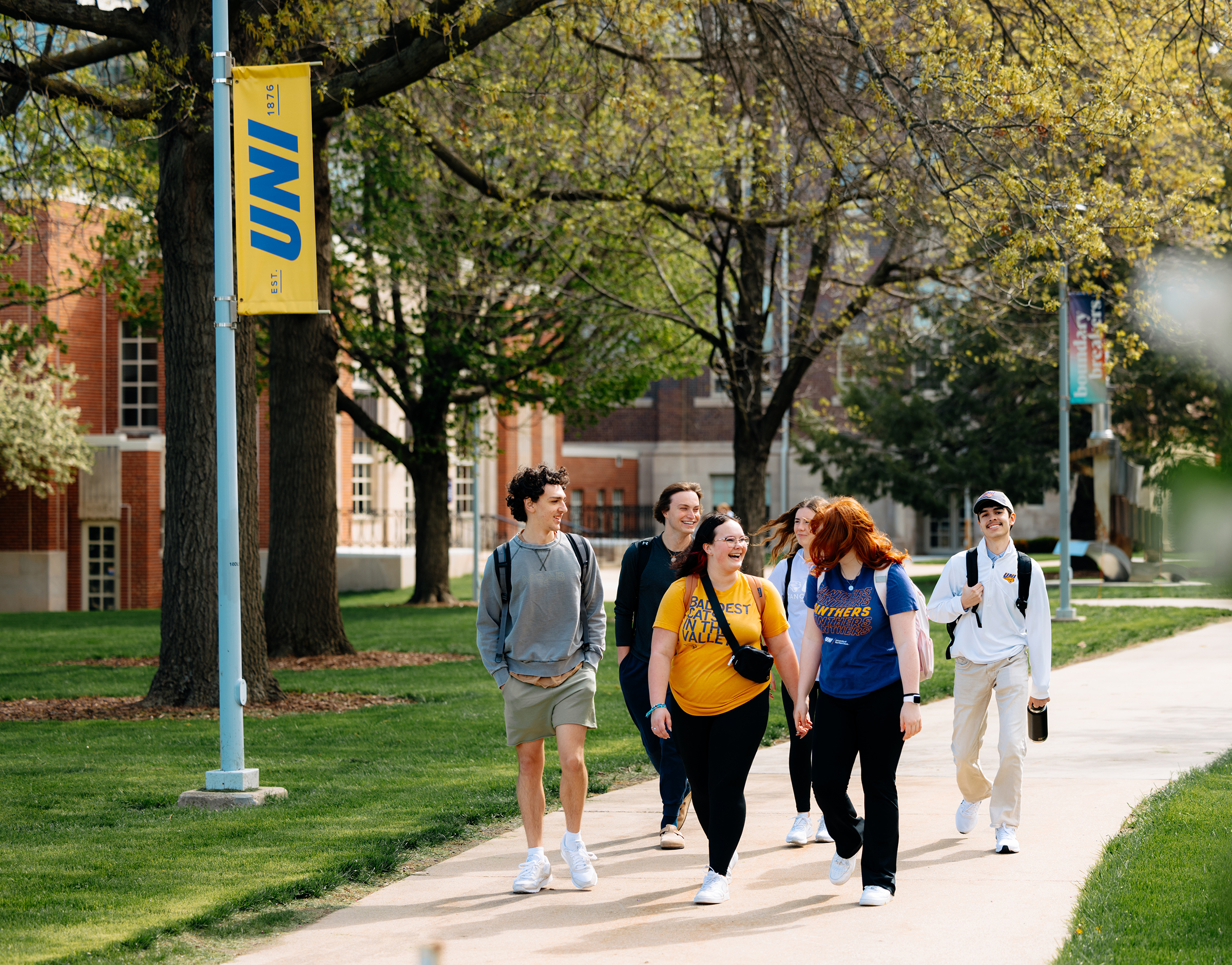 Group of students walking together on campus, smiling and talking, wearing purple and gold UNI attire