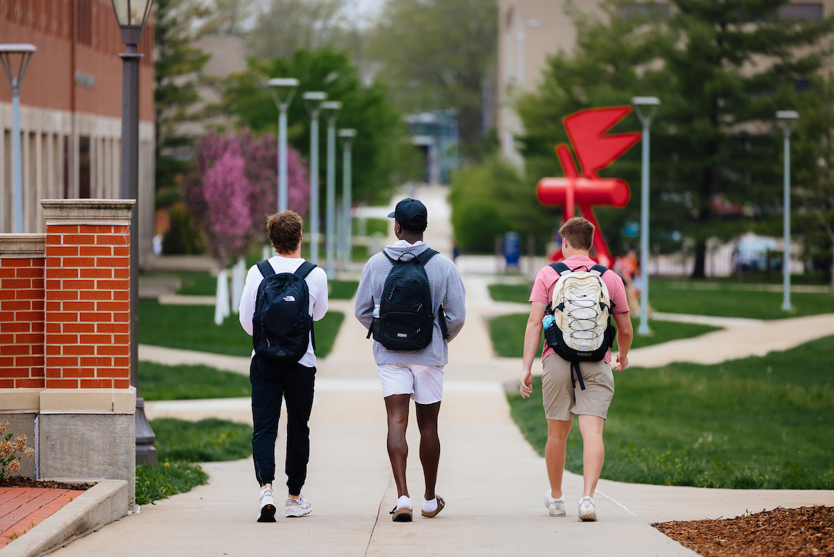 Three students walking away down a campus sidewalk
