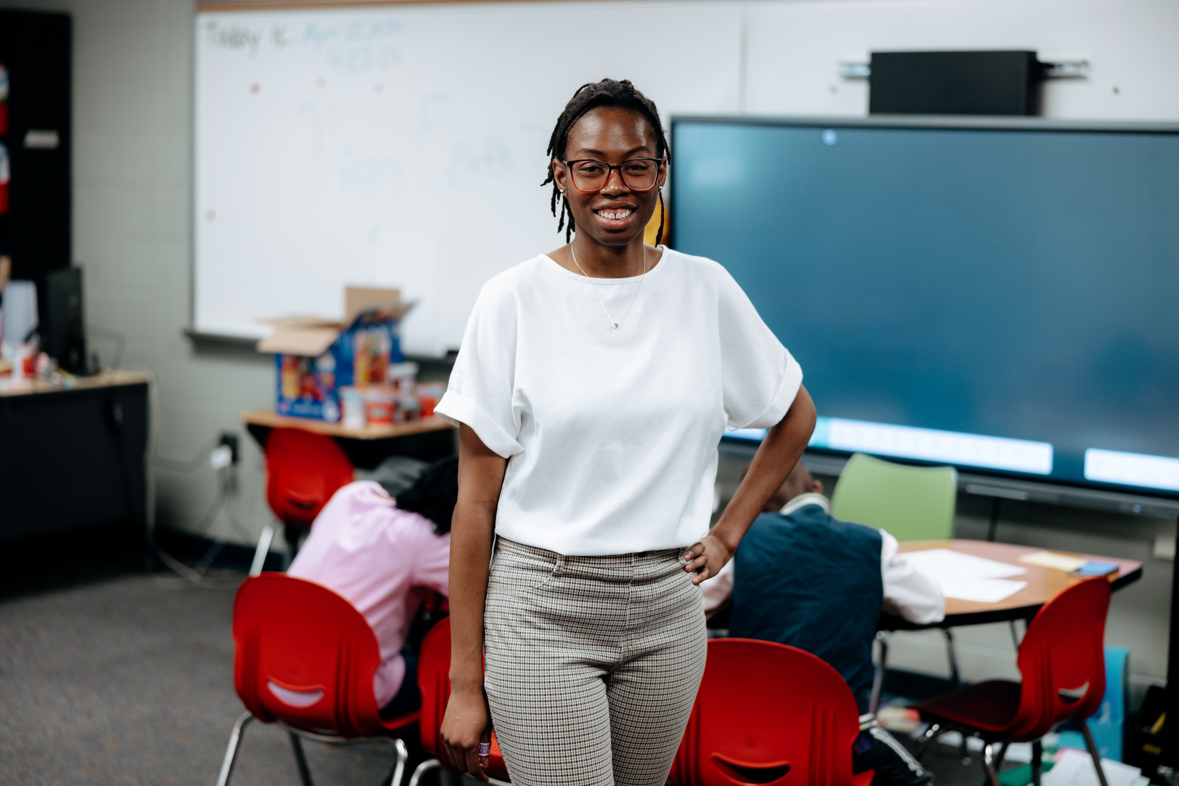 Student teacher standing with students sitting at a table in the background.