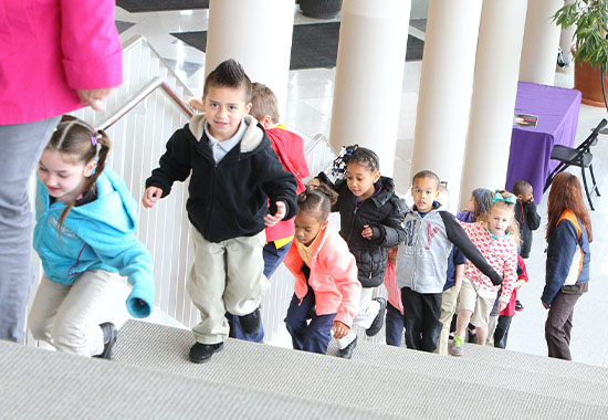 Elementary school students smiling and walking single-file up the stairs at Gallagher Bluedorn