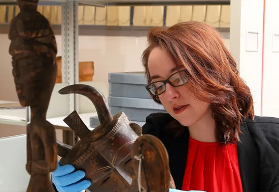 A museum historian wears blue gloves and looks closely at an artifact